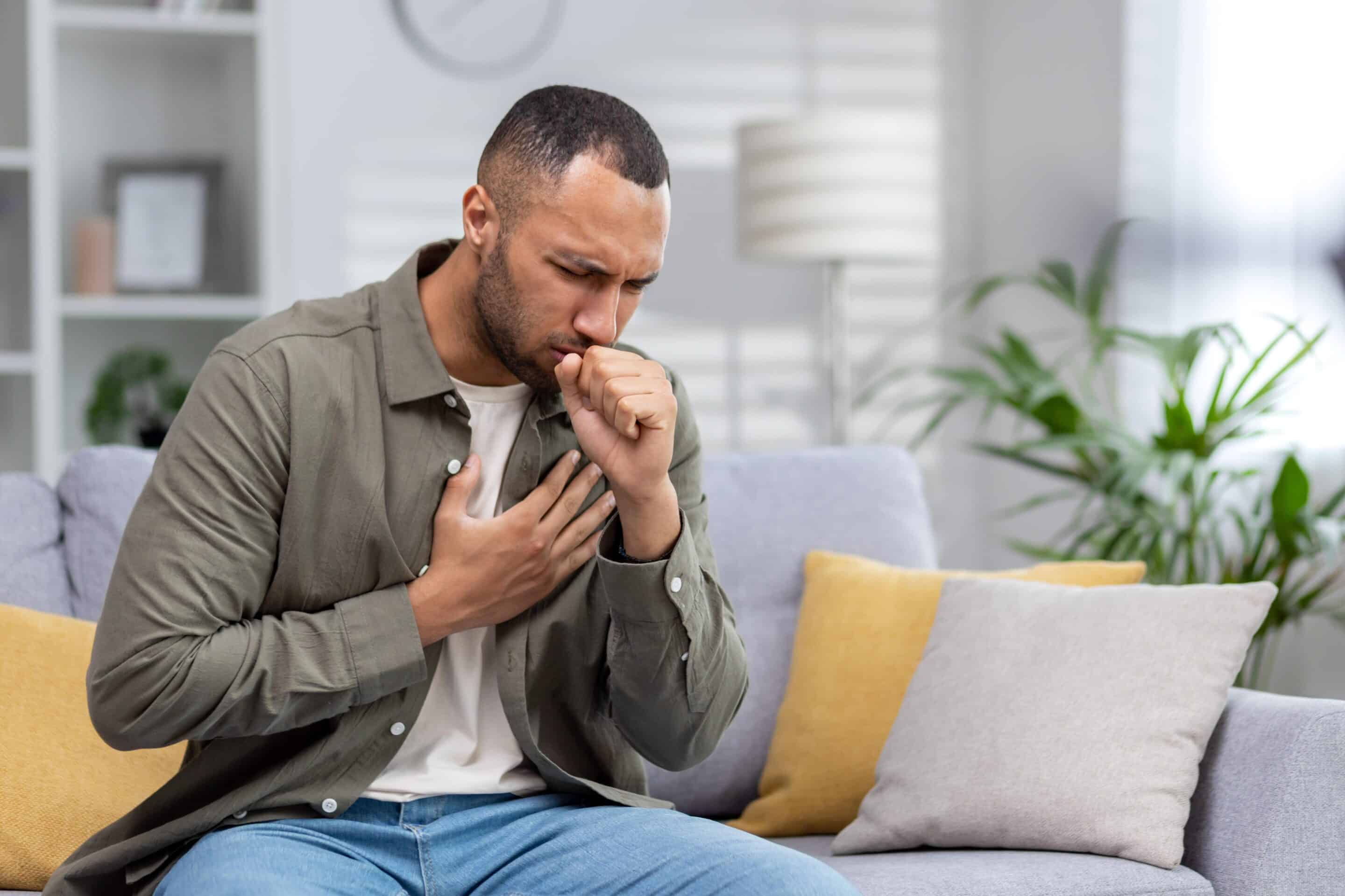 Respiratory Man sitting on the couch at home and coughing.